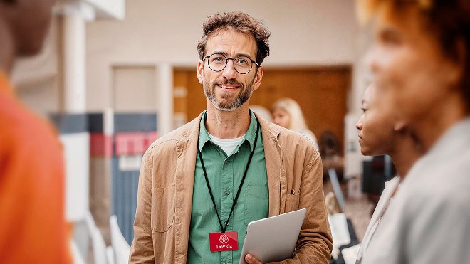 Un partenaire Dovida avec lunettes et ordinateur portable s’entretenant avec des collègues lors d'un événement. Il porte un badge avec le logo Dovida.